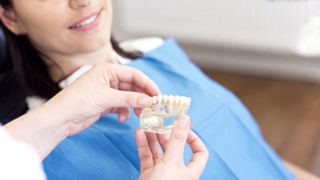 Patiente en consultation avec un dentiste présentant un modèle de prothèse dentaire - Soins de dentisterie esthétique Odontys