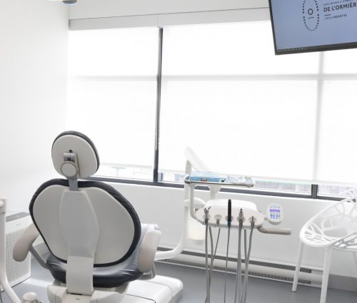 Salle de traitement dentaire moderne et lumineuse avec fauteuil, équipements et écran affichant le logo du Centre dentaire de L'Ormière Odontys.
