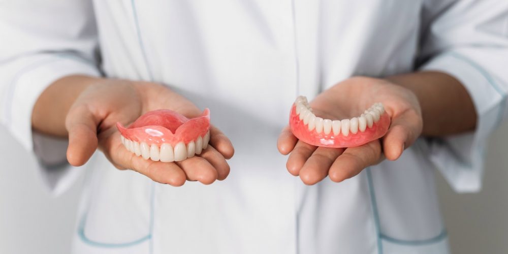 The dentist is holding dentures in his hands. Dental prosthesis in the hands of the doctor close-up. Front view of complete denture. Dentistry conceptual photo. Prosthetic dentistry. False teeth